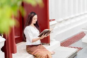 mulher budista asiática usando vestido tradicional da tailândia lendo livro de dharma, santuário ratchanatdaram bangkok. foto