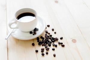 grãos de café e xícara de café quente em fundo de madeira foto