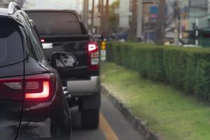 parte traseira do carro preto na estrada de asfalto em direção ao objetivo da viagem. viajando a trabalho na hora do rush. ambiente de turva de outros carros na cidade. ilha de grama verde ao lado. foto