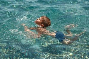 menino criança aprendendo a nadar no mar claro e transparente. foto