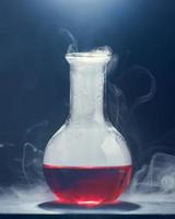 frasco de vidro com um líquido vermelho fuma sobre um fundo cinza. foto