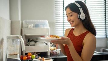 bela jovem cozinhando na cozinha em casa enquanto ouve música através de fones de ouvido - conceitos de estilo de vida foto