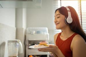 bela jovem cozinhando na cozinha em casa enquanto ouve música através de fones de ouvido - conceitos de estilo de vida foto