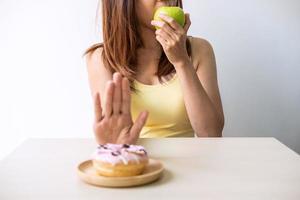 jovem mulher saudável usando a mão empurrar sobremesa e doces e escolher maçã verde, estilo de vida saudável e conceito de dieta foto