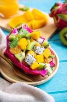 misture a salada de frutas tropicais servida em metade de uma fruta do dragão na mesa de madeira foto