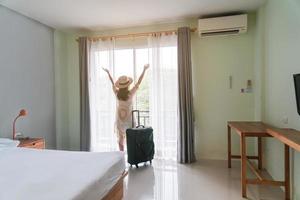 jovem viajante com bagagem olhando a vista no quarto de hotel nas férias de verão foto