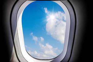 céu azul e vista do sol com nuvens brancas vistas de dentro de uma janela de avião, conceito de viagens e transporte aéreo foto