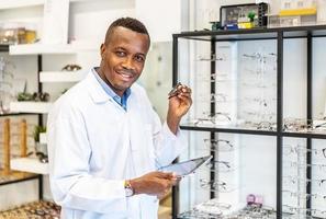 conceito de visão e visão. vista do oculista atraente americano africano sorridente trabalhando com tablet em sua loja de óculos. foto