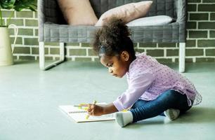menina negra afro-americana bonitinha desenhando no chão dentro de casa, pessoas africanas - crianças foto