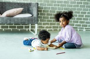 menina afro-americana bonita e livro de desenho de menino no chão dentro de casa, pessoas africanas - crianças foto