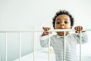 menino afro-americano fica perto da cama e ele parece feliz e inocente. conceito de emoção de felicidade ocorre com boa saúde e apoio da família. foto