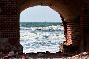 mar azul ondas marinha através do arco de tijolos vermelhos, vista do antigo forte de tijolos pelo mar báltico foto