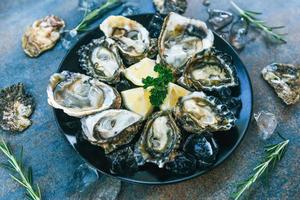 ostras frescas frutos do mar em um fundo de placa preta - concha de ostra aberta com ervas especiarias limão alecrim servido mesa e gelo frutos do mar saudáveis jantar de ostras cruas no restaurante comida gourmet foto