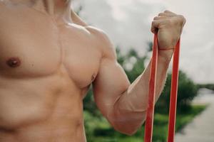 homem forte irreconhecível tem treino com banda de resistência, fica mais forte a cada dia, mostra corpo bem construído, poses ao ar livre. esporte, musculação e conceito de estilo de vida saudável. atleta sem rosto foto