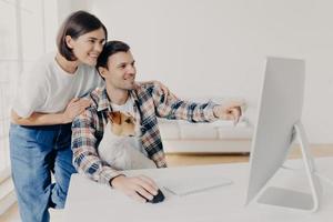 homem feliz e sua namorada consultam sobre o projeto futuro, apontam para o monitor, posam no local de trabalho junto com o cachorro no interior da casa, assistem ao vídeo tutorial on-line, passam o tempo no apartamento moderno foto