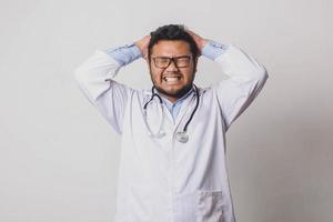 médico masculino com expressão frustrada, segurando a cabeça com as duas mãos isoladas no fundo branco foto