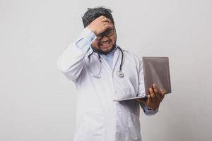 médico masculino com expressão estressada e exausta segurando laptop isolado no fundo branco foto