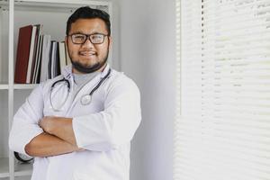 médico masculino pensativo em pé e cruzando os braços no hospital foto