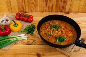 ensopado com carne e legumes em molho de tomate em fundo de madeira foto