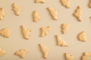 padrão de cookies em forma de vista superior de dinossauros em um fundo bege. foto monocromática