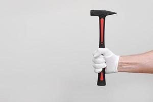 mão masculina na luva branca protetora segurando o martelo vermelho isolado no fundo branco. reparação e renovação de casas ou automóveis, equipamentos industriais foto