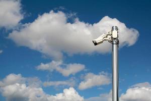 câmeras de segurança ao ar livre em um poste com fundo azul céu nublado foto