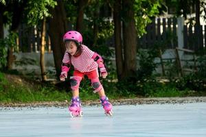 menina asiática bonitinha em almofadas protetoras e capacete de segurança praticando patinação no parque. emocionantes atividades ao ar livre para crianças. foto