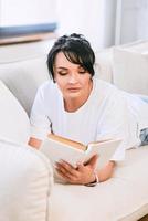 mulher bonita no sofá lendo o livro. tempo livre, educação, conceito de autodesenvolvimento. foto