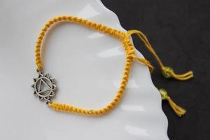 pulseira trançada artesanal amarela com chakra manipura na borda de um prato branco como a neve foto