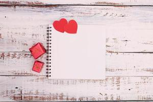 coração de papel com caixa vermelha e livro no chão de madeira foto