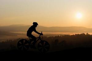 silhuetas homem e bicicleta na montanha à luz do sol foto