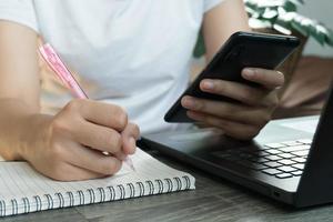 mulher de negócios jovem sentado à mesa com o laptop e tomando notas no caderno. foto