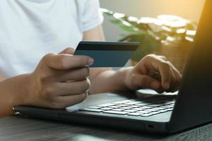 mãos segurando o cartão de crédito e usando o laptop. compras online. trabalhar em casa conceito foto