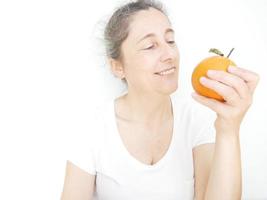 mulher de quarenta e nove anos em uma camiseta branca contra um fundo branco com uma laranja foto