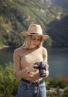 fotógrafo turista viajante em pé no topo verde na montanha segurando nas mãos a câmera fotográfica digital foto