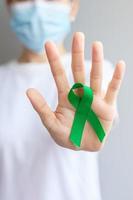 mão segurando a fita verde para fígado, vesícula biliar, ducto biliar, cervical, câncer renal e mês de conscientização do linfoma. conceito de saúde e dia mundial do câncer foto
