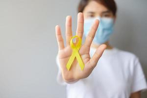 mão segurando a fita amarela para apoiar as pessoas que vivem e estão doentes. setembro dia de prevenção ao suicídio, infância, sarcoma e conceito de mês de conscientização do câncer ósseo foto