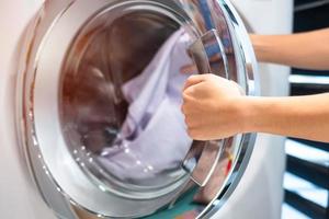 mão de mulher dona de casa segurando roupas dentro da máquina de lavar na lavanderia foto