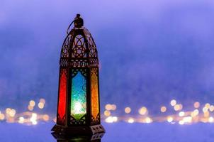 foco seletivo no vidro de cor azul da lanterna com luzes decorando para o ano novo islâmico colocado no fundo da janela com bokeh de gota de chuva. foto