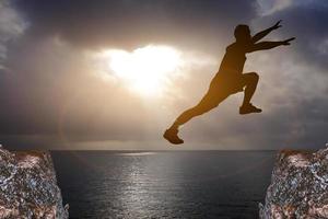 homem silhueta pulando sobre um precipício entre dois mar rochoso ao nascer do sol. liberdade, risco, desafio, conceito de sucesso. foto