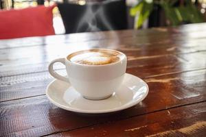 arte com leite em forma de coração em xícara de café branco na mesa de madeira no café restaurante foto