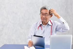 médico impensável, velho chinês usando tablet de computador com confuso complicado com o problema dos problemas de notícias de quebra-cabeça de saúde do vírus corona. foto