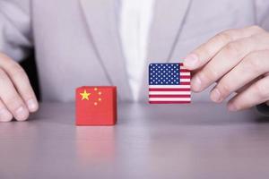 guerra comercial dos eua e da china, conflito de interesses. bandeiras da américa e da china em cubos de madeira na mão de um empresário. foto