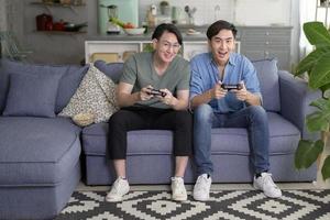 jovem casal gay sorridente jogando videogame na sala de estar em casa, lgbtq e diversidade foto