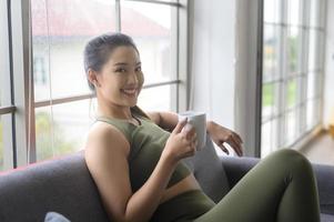 mulher jovem fitness em roupas esportivas tomando uma xícara de café depois de se exercitar em casa, saudável e estilos de vida. foto