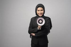 feliz mulher muçulmana está anunciando com megafone em fundo branco foto