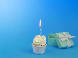cupcake doce com vela de proa e caixa de presente em fundo azul com espaço de cópia. conceito de fundo de festa de aniversário feliz. foto