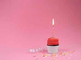 doce bolinho vermelho com vela de laço no fundo rosa com espaço de cópia. conceito de fundo de festa de aniversário feliz. foto