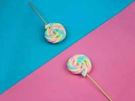 doces coloridos de pirulito de merengue de cor de arco-íris em meio fundo azul e rosa. conceito de sobremesa doce de verão bonito. foto