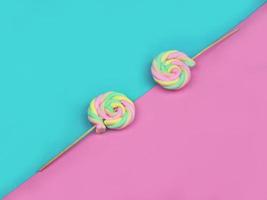 doces coloridos de pirulito de merengue de cor de arco-íris em meio fundo azul e rosa. conceito de sobremesa doce de verão bonito. foto